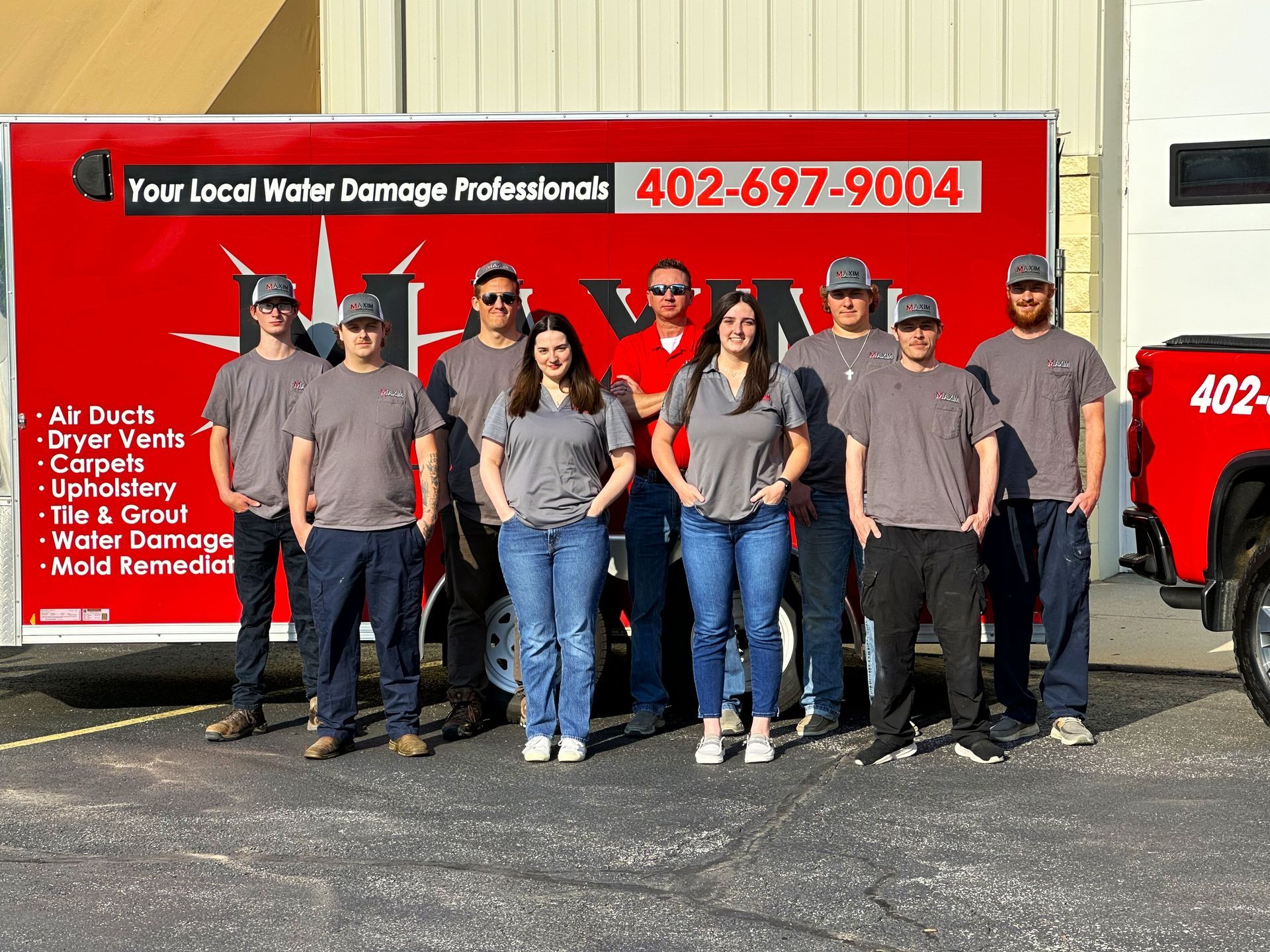 Group of people in gray shirts and hats in front of a red truck with 