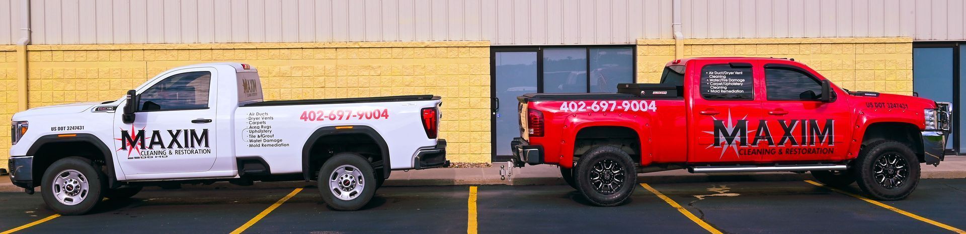 Two trucks, white and red, parked near a yellow and beige building. Both trucks have 