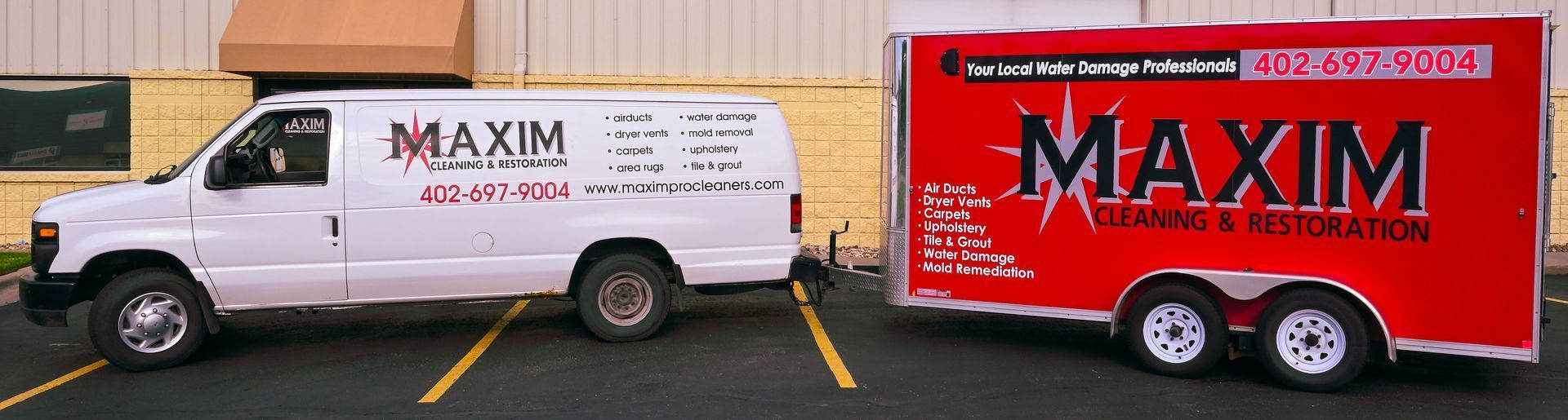 White Maxim van towing a red Maxim trailer, both branded for cleaning and restoration services, parked outside.