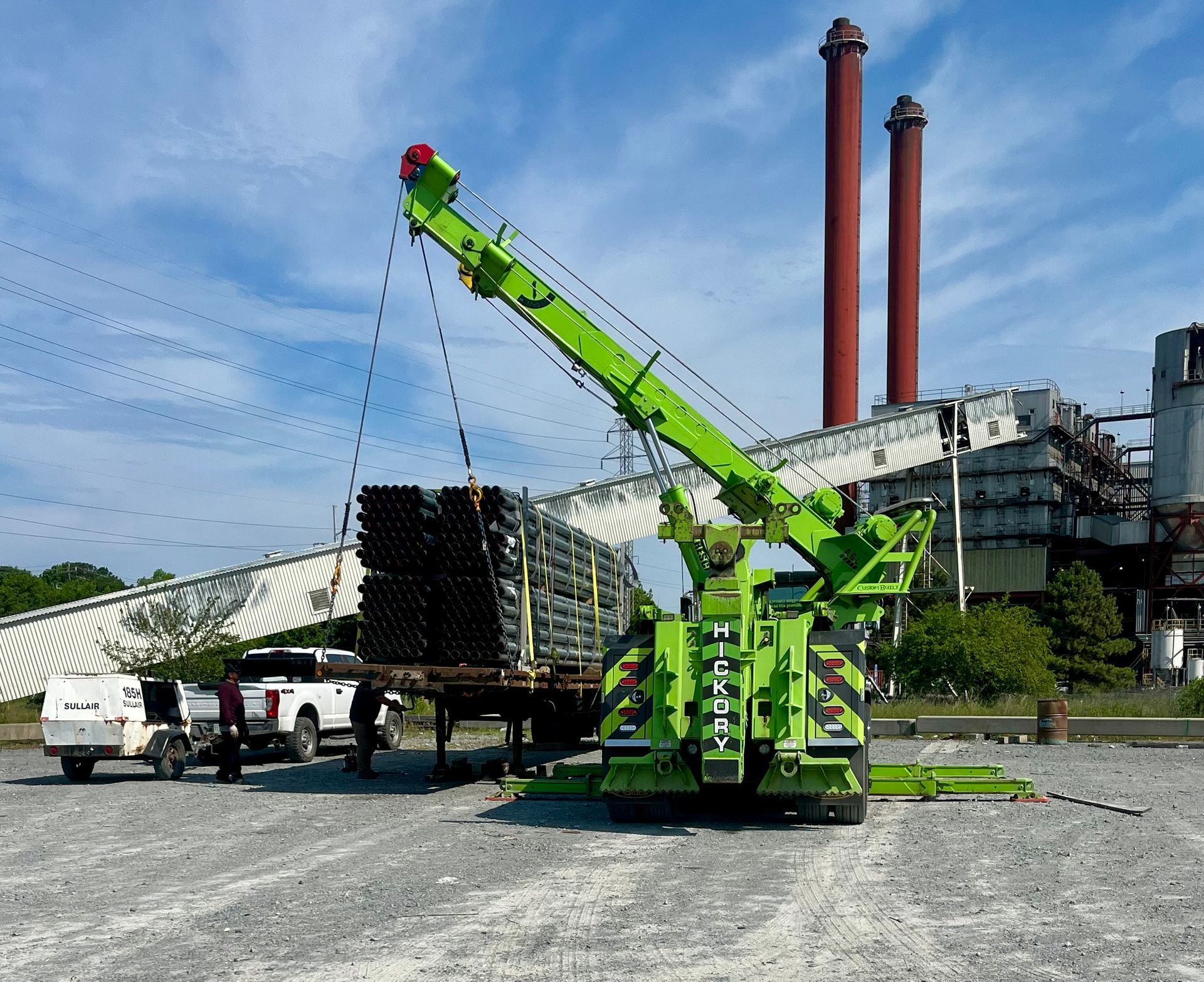 A green crane is lifting a stack of pipes.