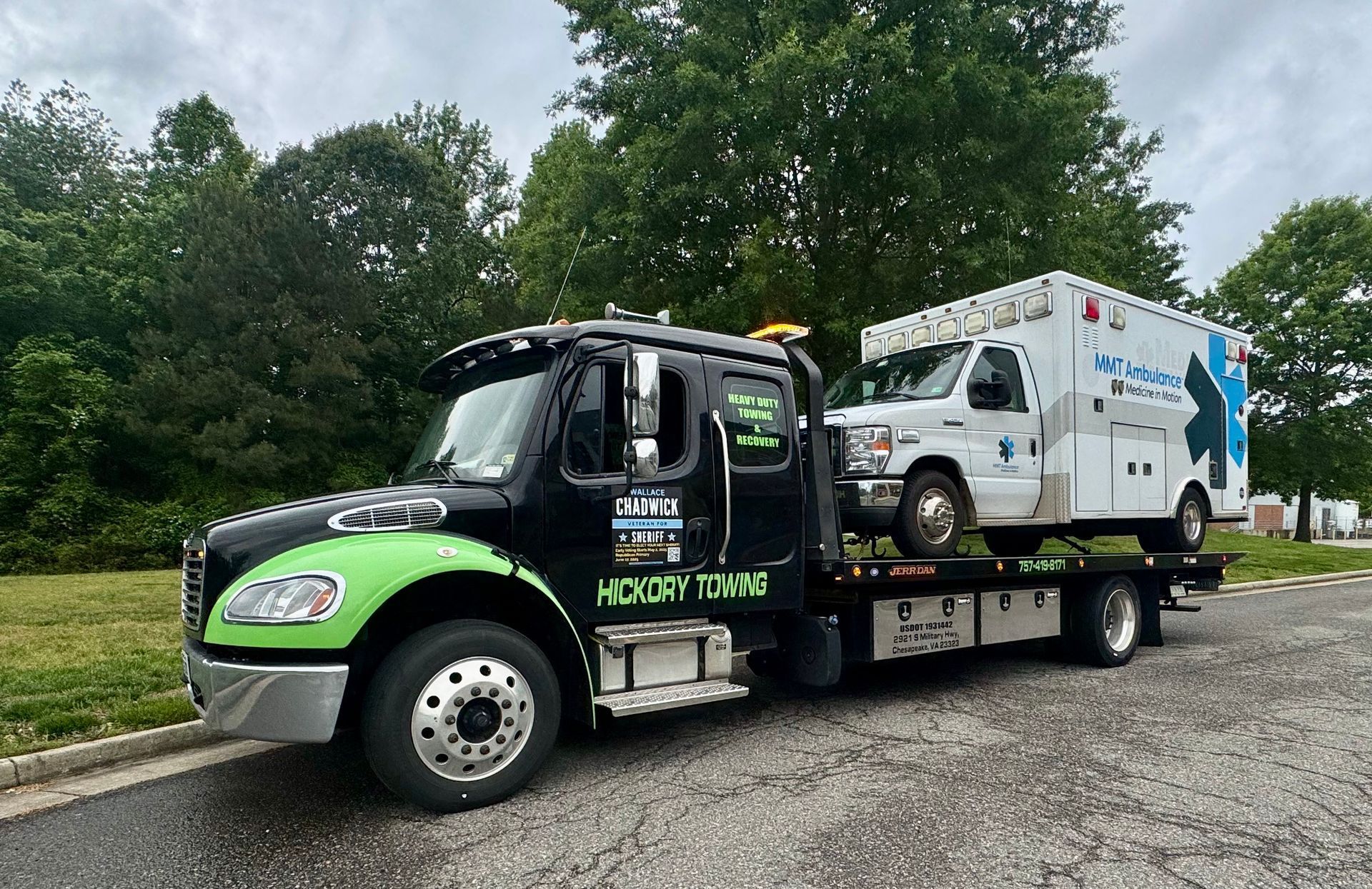 A tow truck with an ambulance on the back is parked on the side of the road.