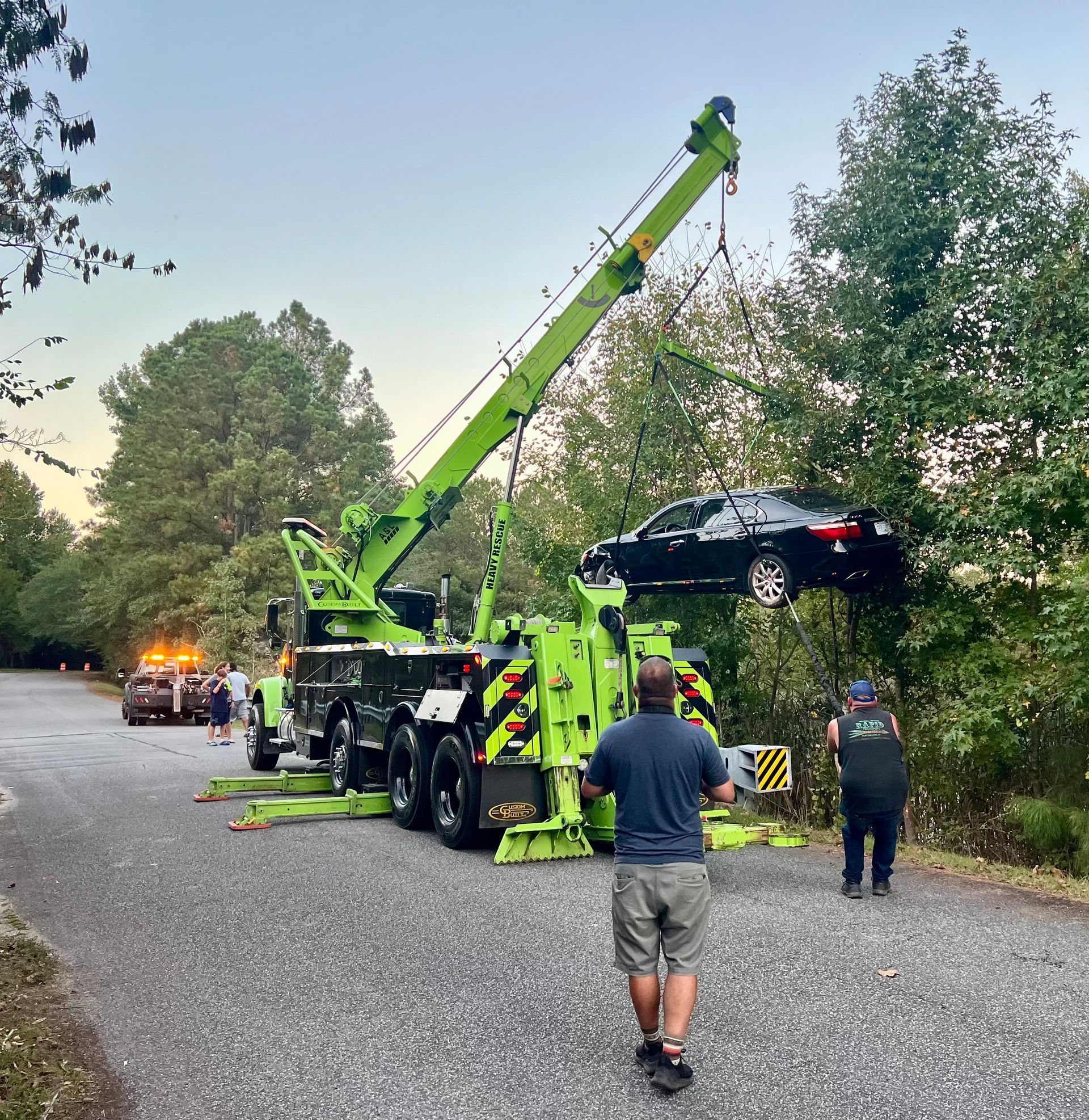 A car is being lifted by a green tow truck.