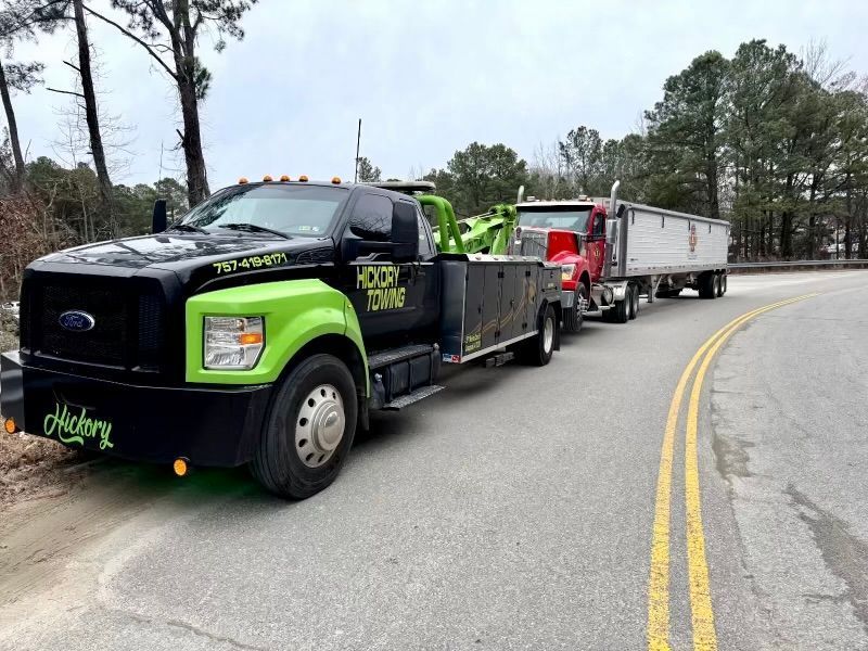 A green tow truck is driving down a road next to a red truck.