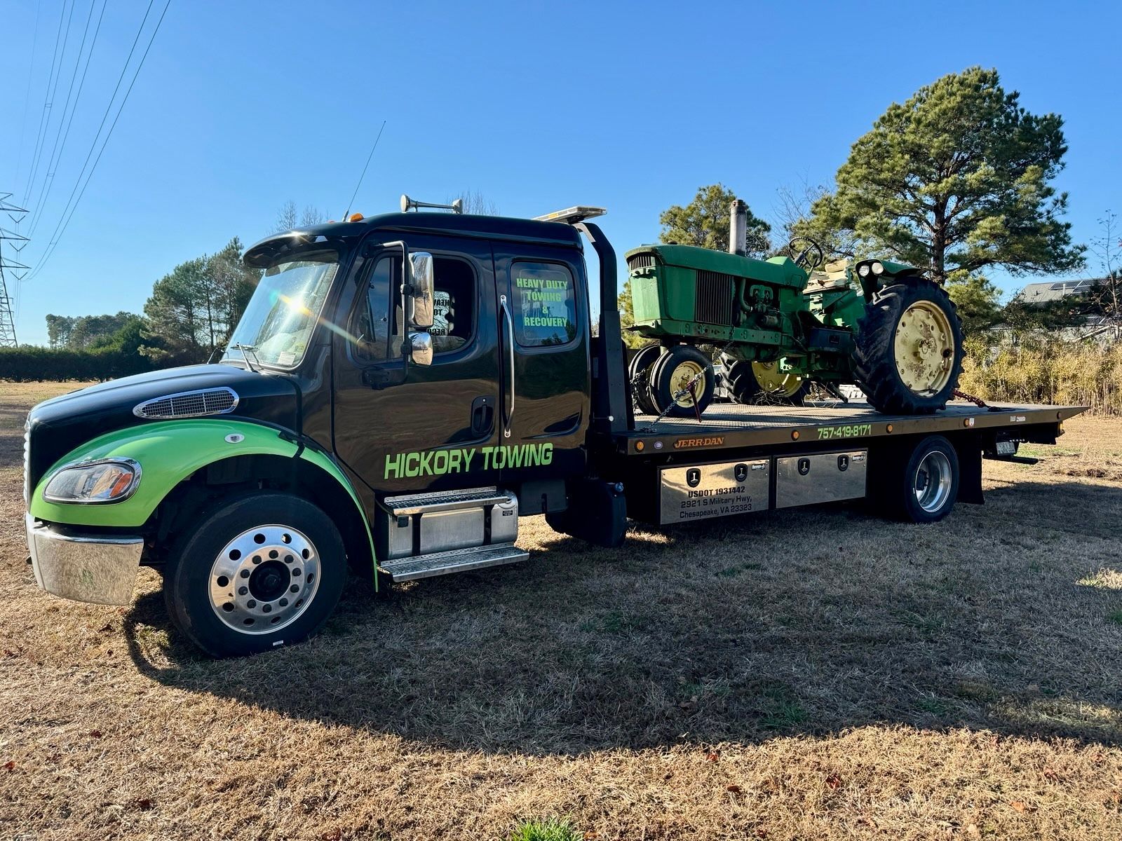 A green tractor is being towed by a tow truck.