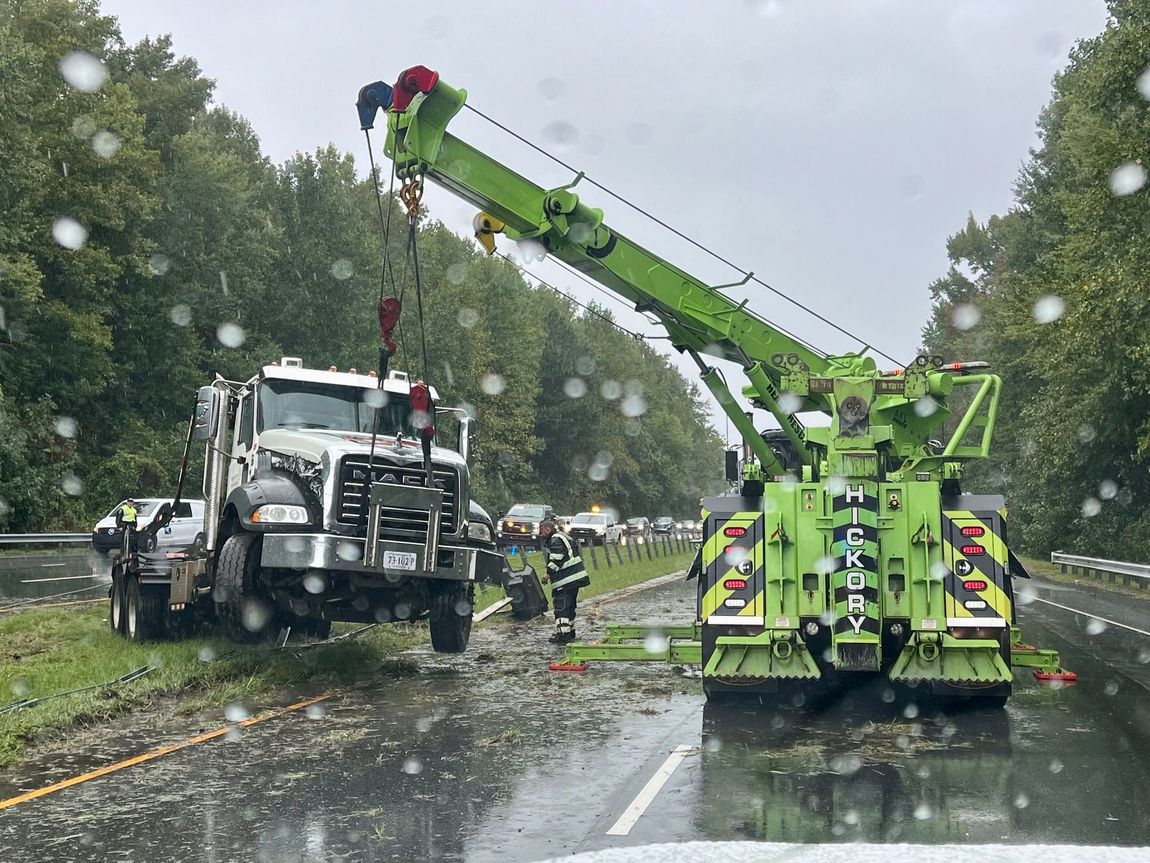 A truck is being towed by a crane on the side of the road.