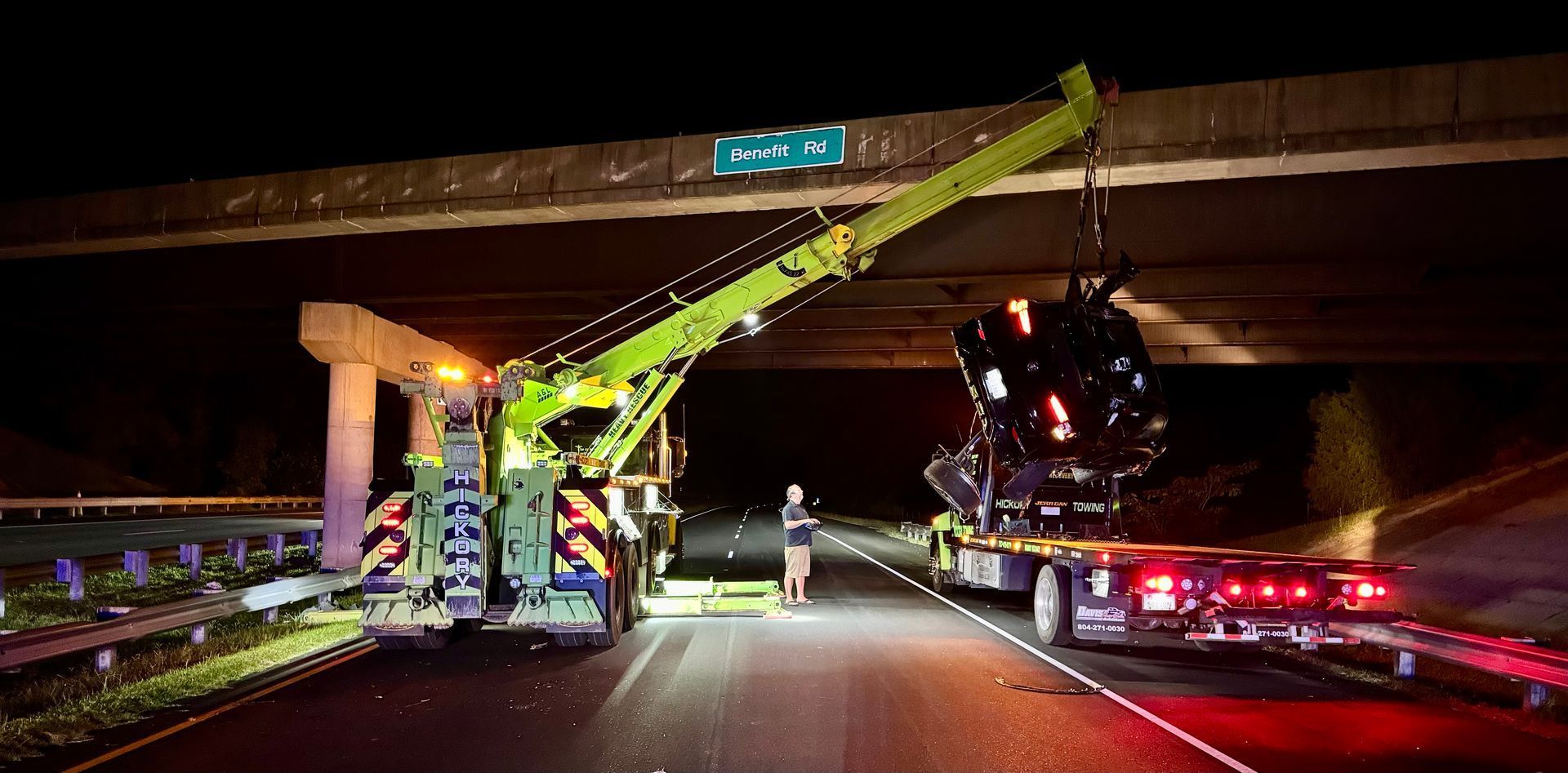 A truck is towing a car under a bridge at night.