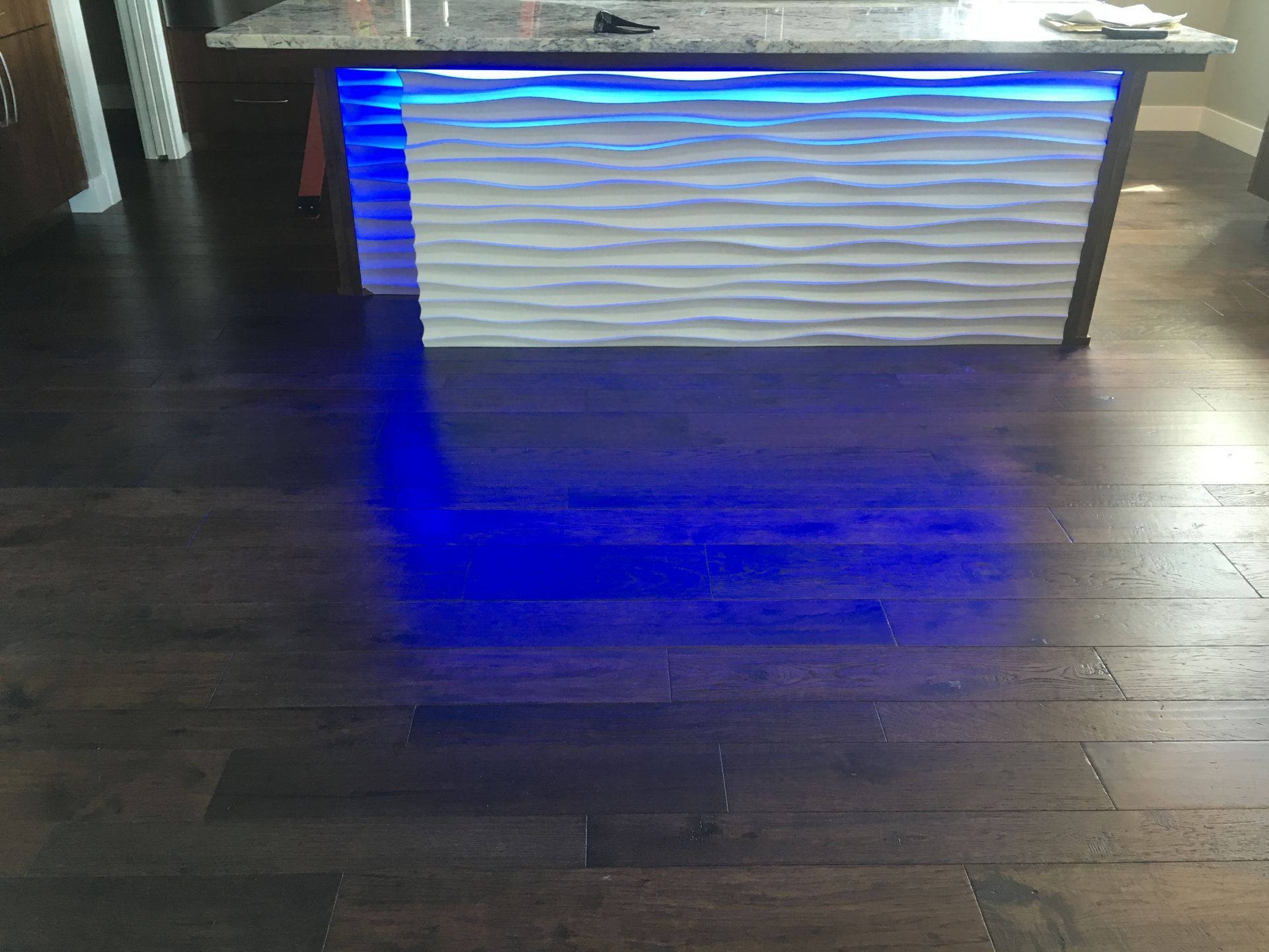 A blue light is shining on a wooden floor in a kitchen.
