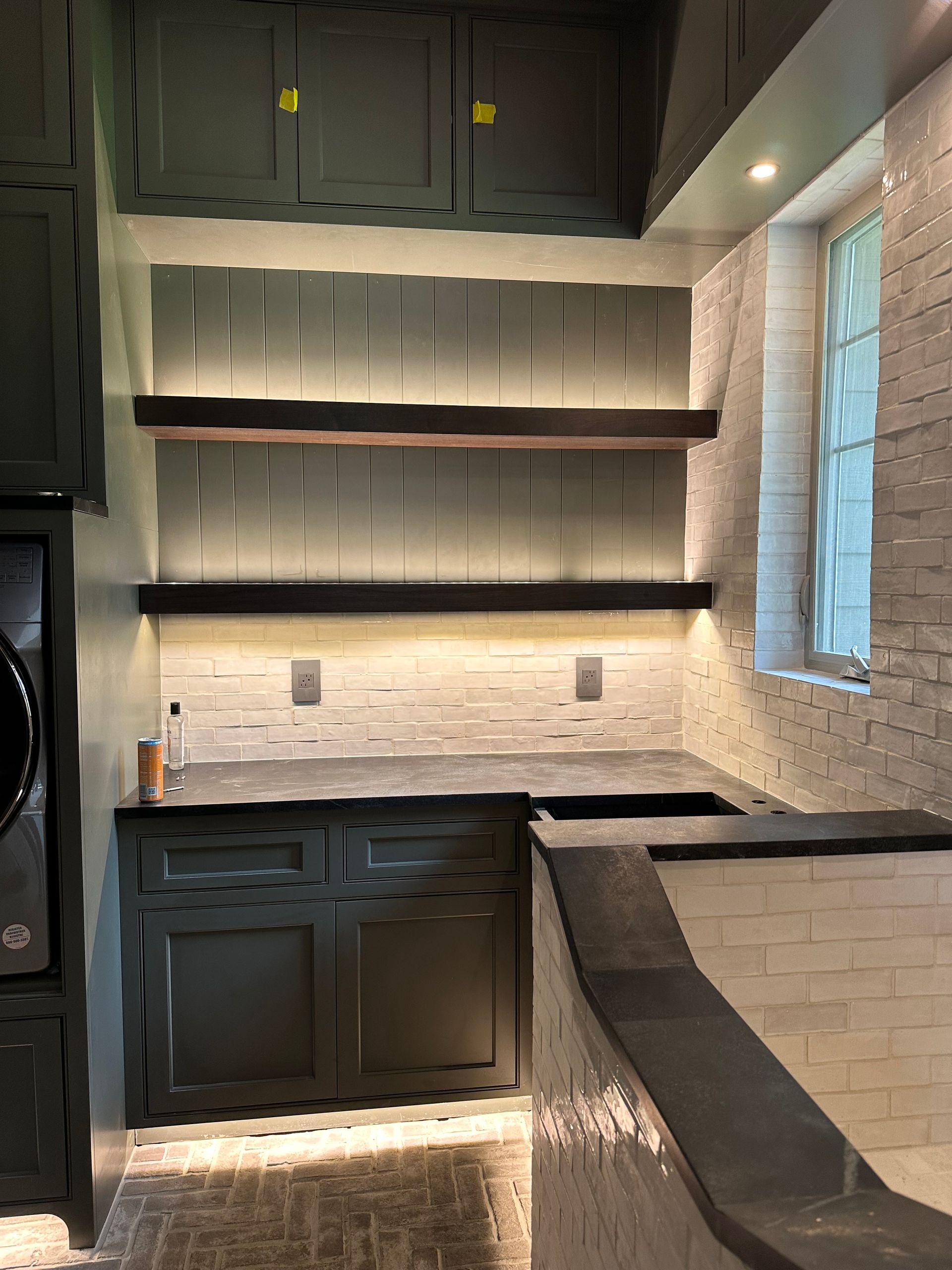 A kitchen with a washing machine , sink , and shelves.
