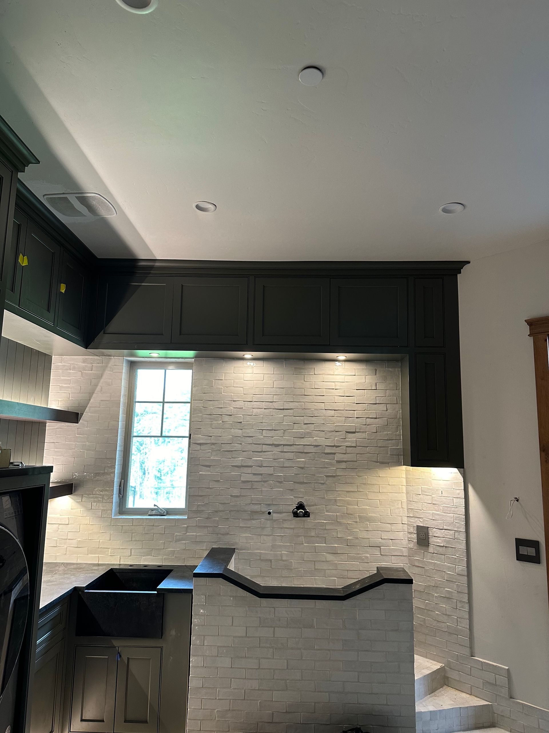 A kitchen with black cabinets and white brick walls.