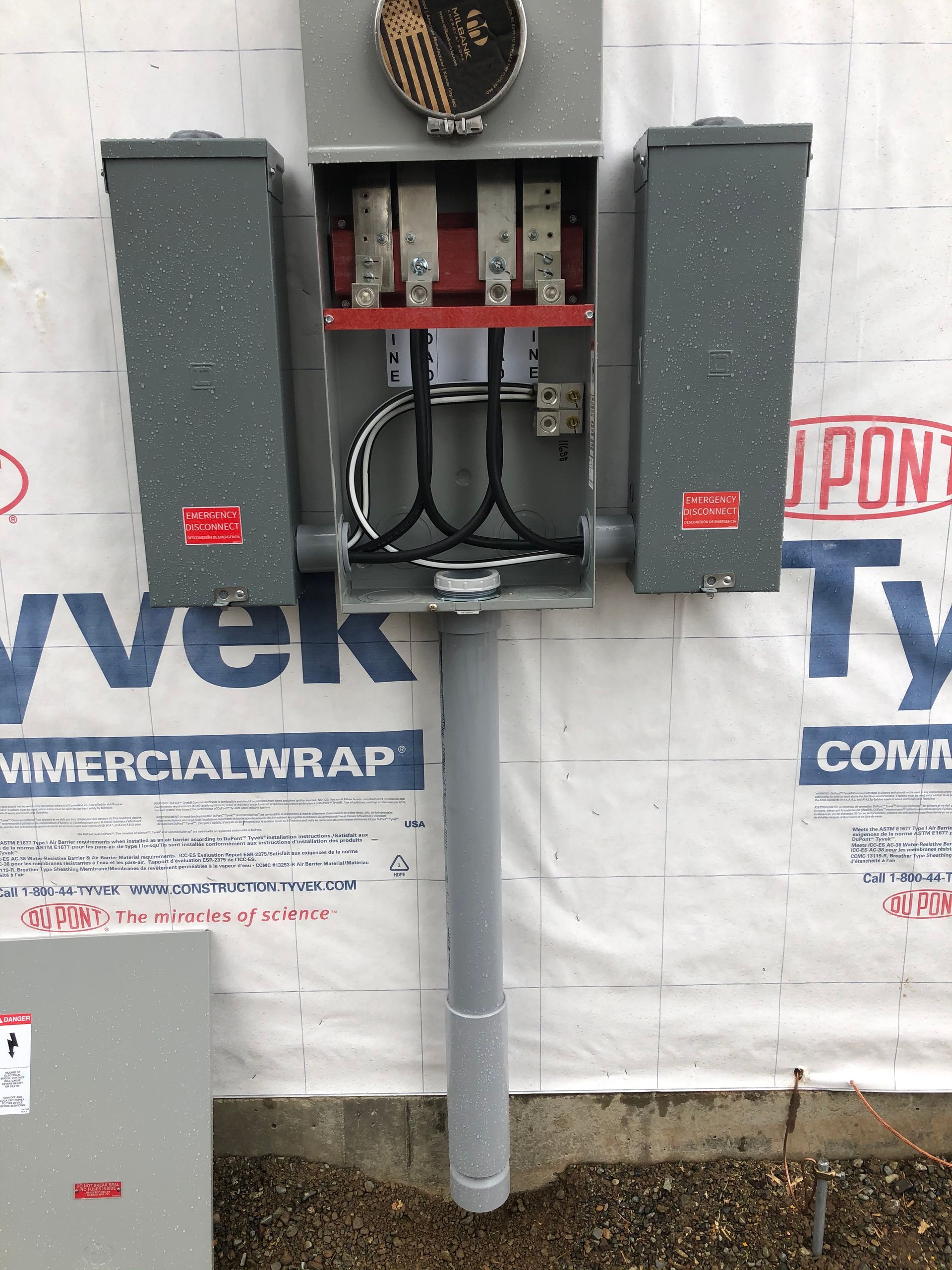 An electrical box is sitting on top of a pole in front of a wall covered in vek commercial wrap.