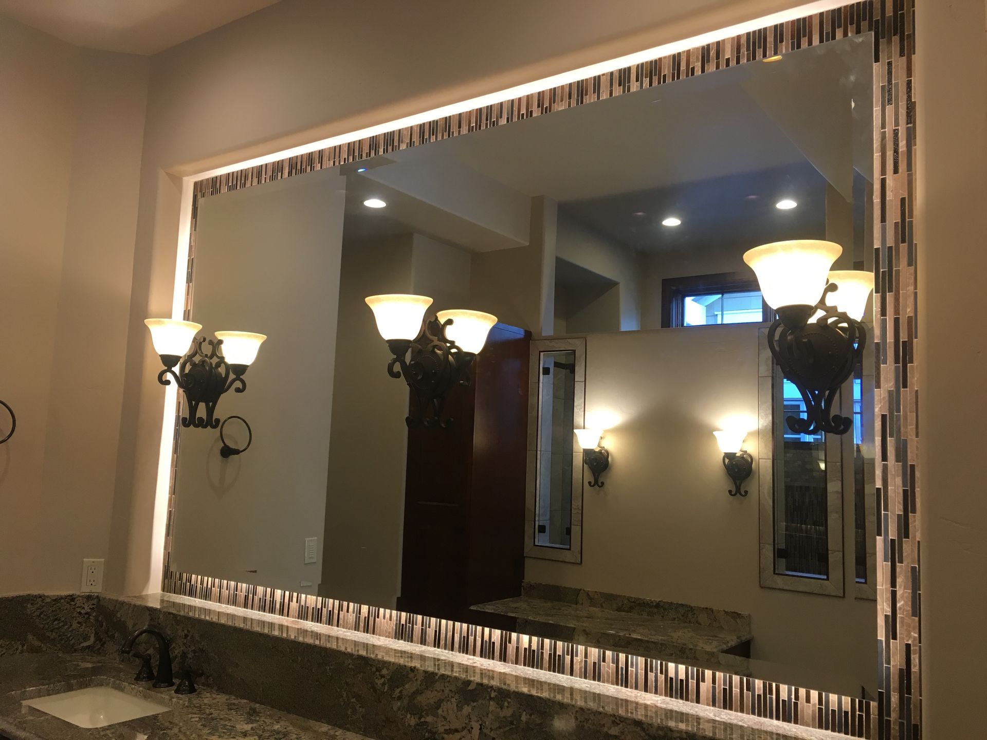 A bathroom with a large mirror and lamps on the wall.