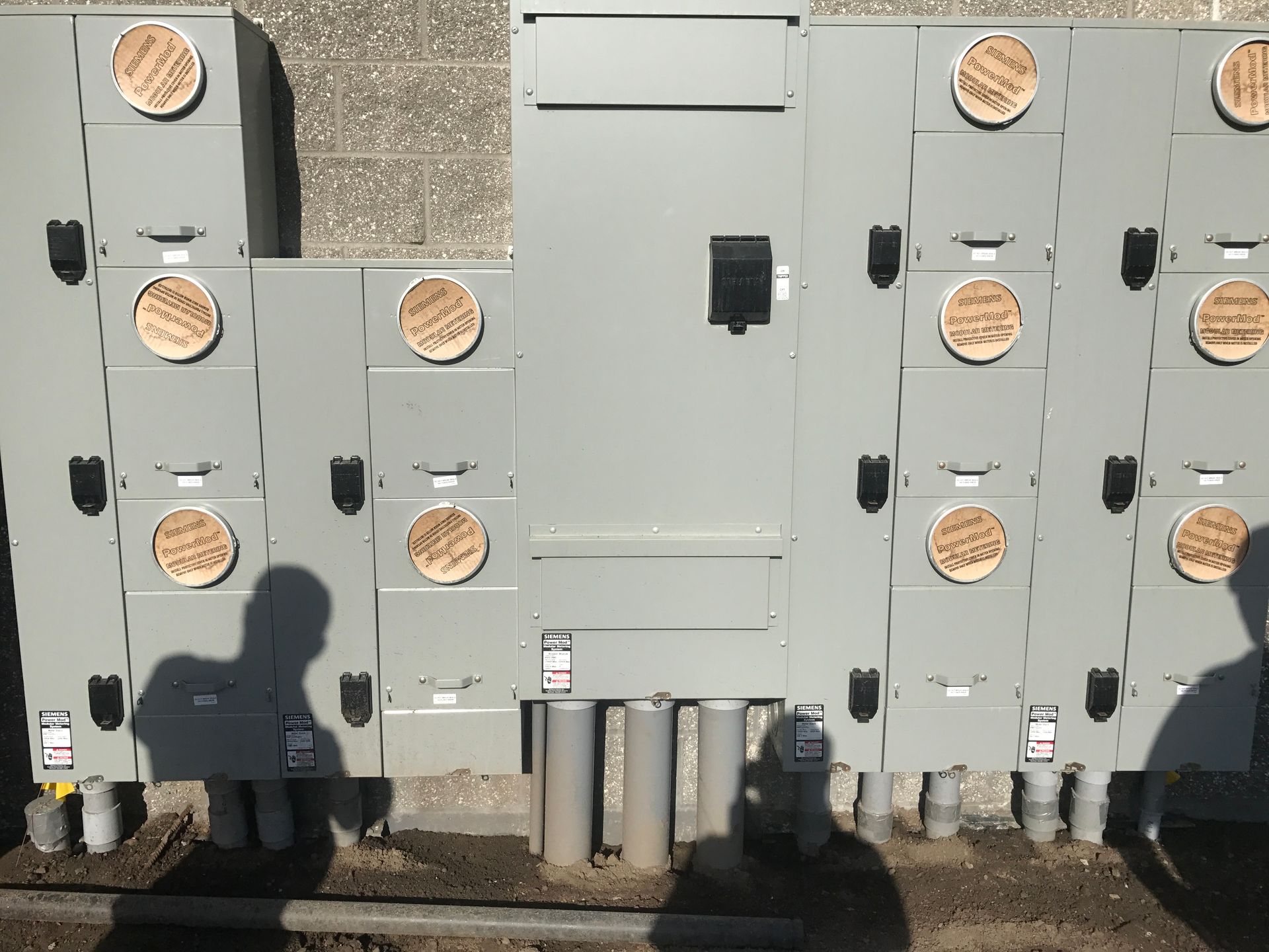 A row of electrical boxes are lined up against a brick wall.