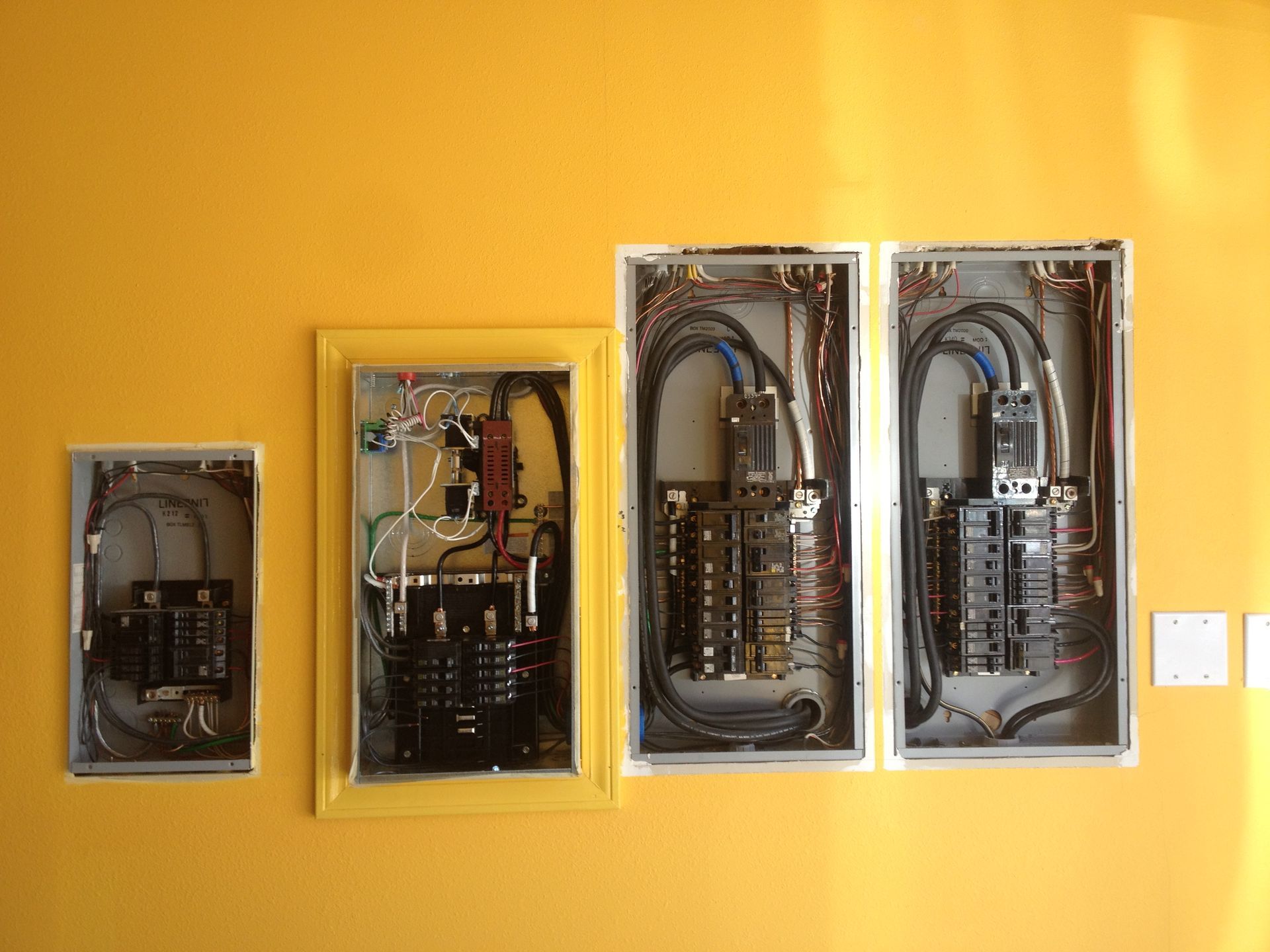 Four electrical boxes are lined up on a yellow wall.