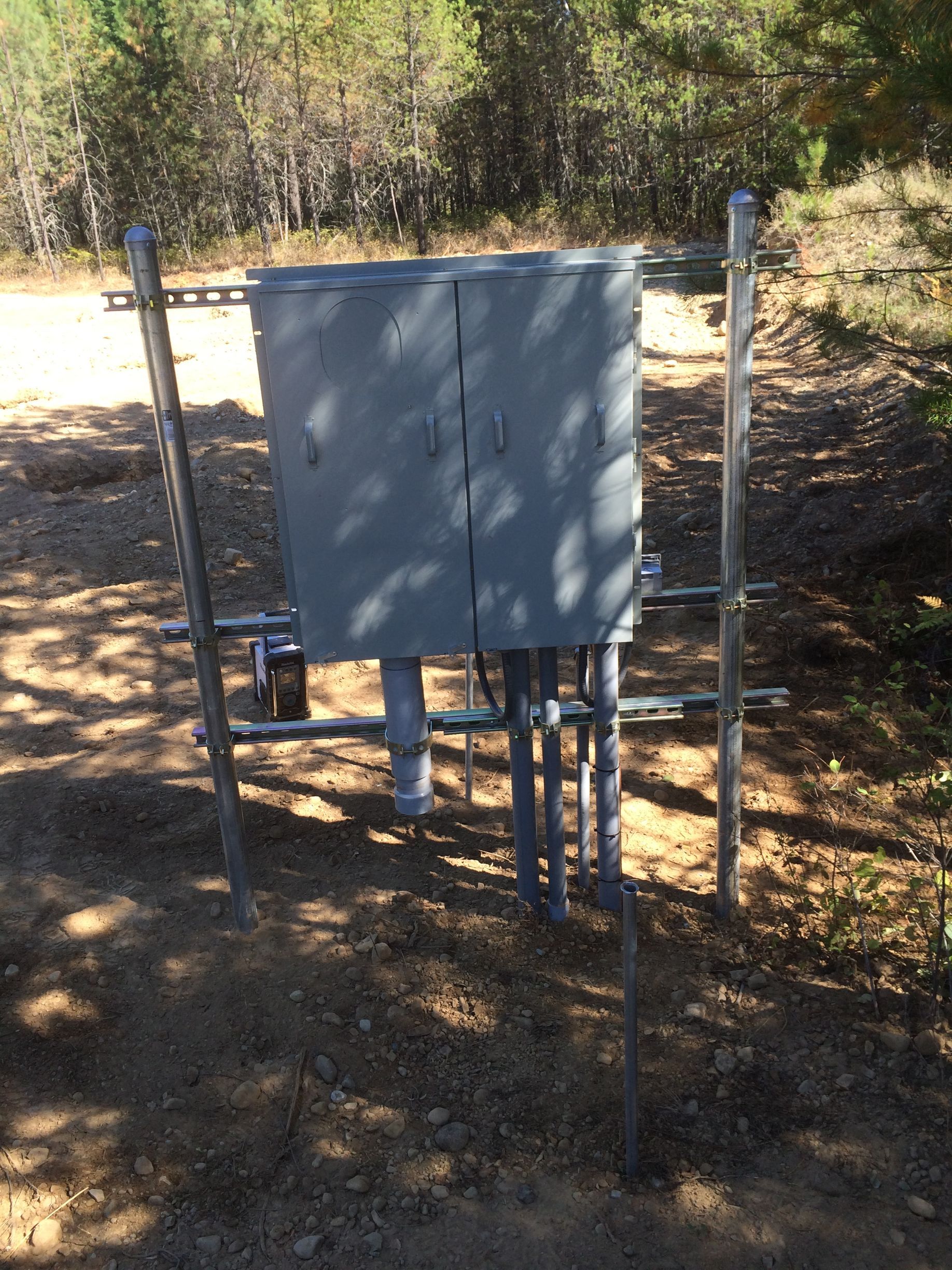 A metal box is sitting in the dirt next to a fence