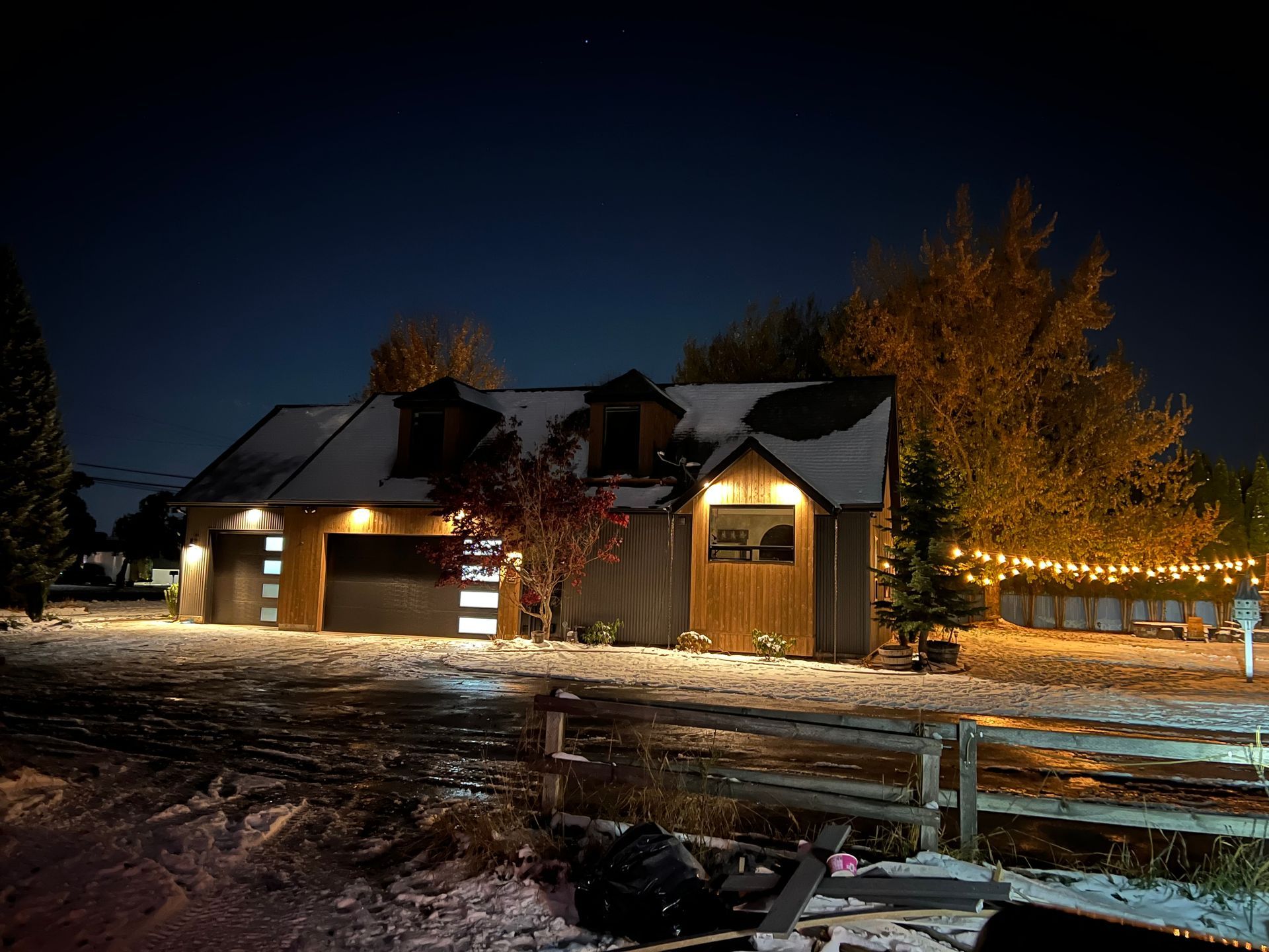 A house with a garage and a fence is lit up at night.