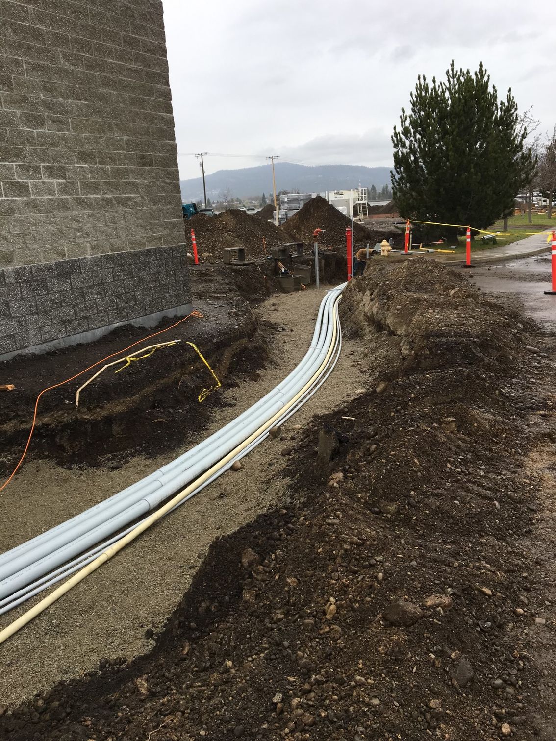 A bunch of pipes are laying in the dirt in front of a building.