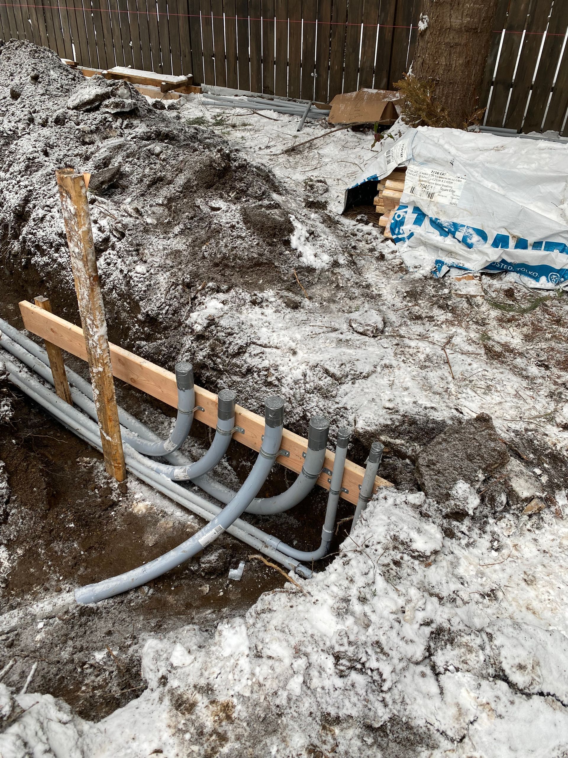 A bunch of pipes are laying in the dirt in the snow.