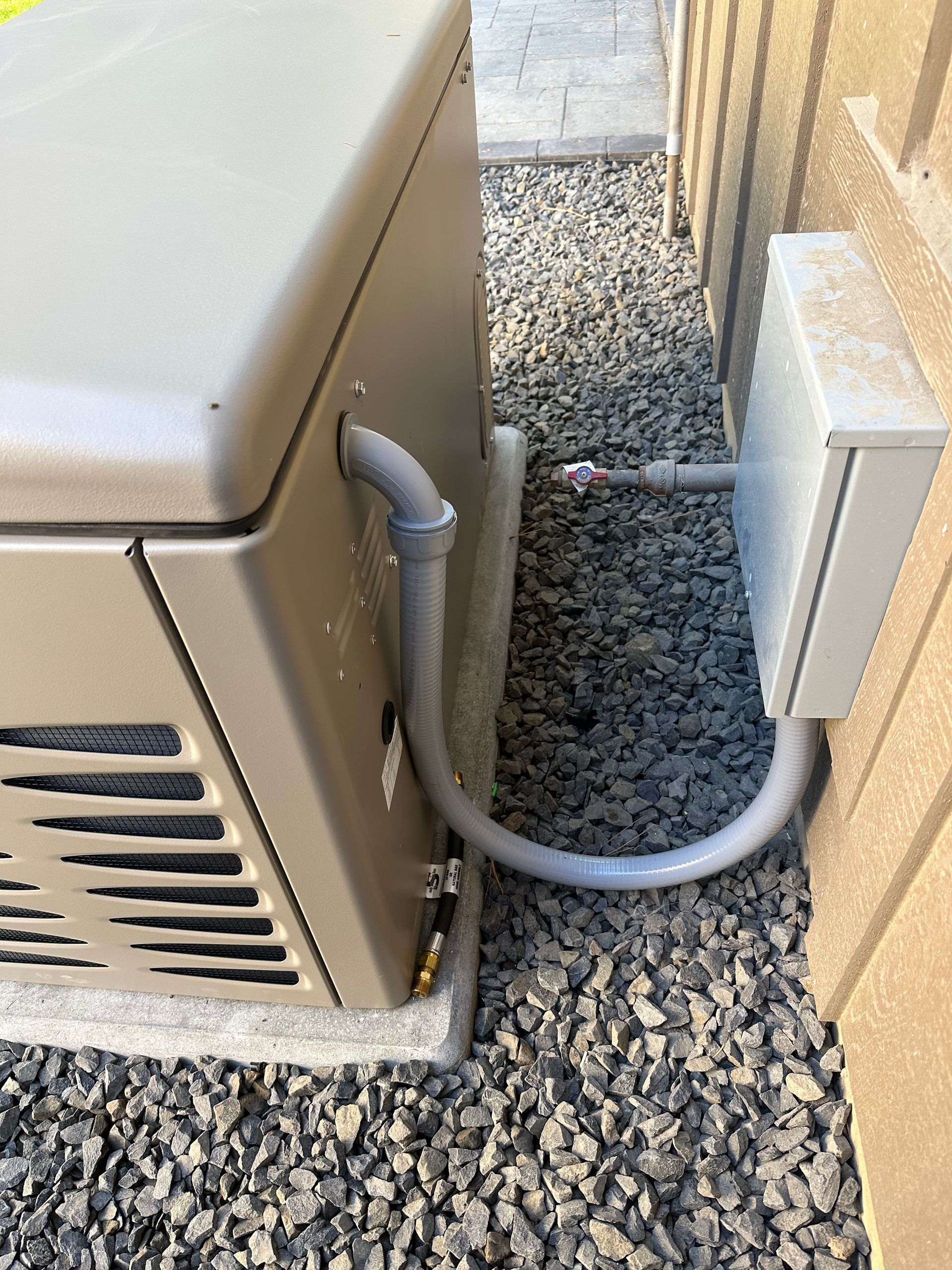 A generator is connected to a box on the side of a building.