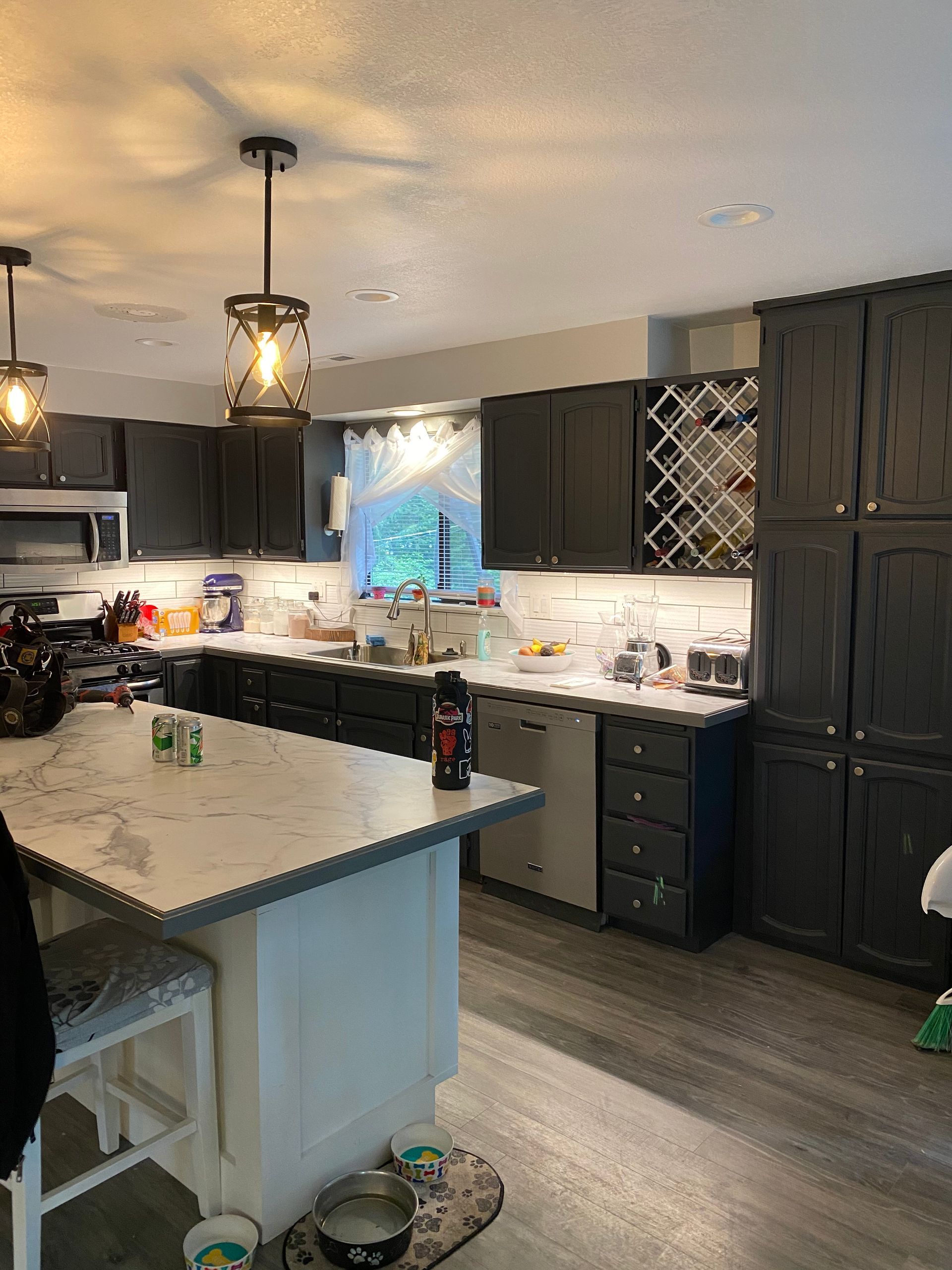 A kitchen with black cabinets , white counter tops , stainless steel appliances and a large island.