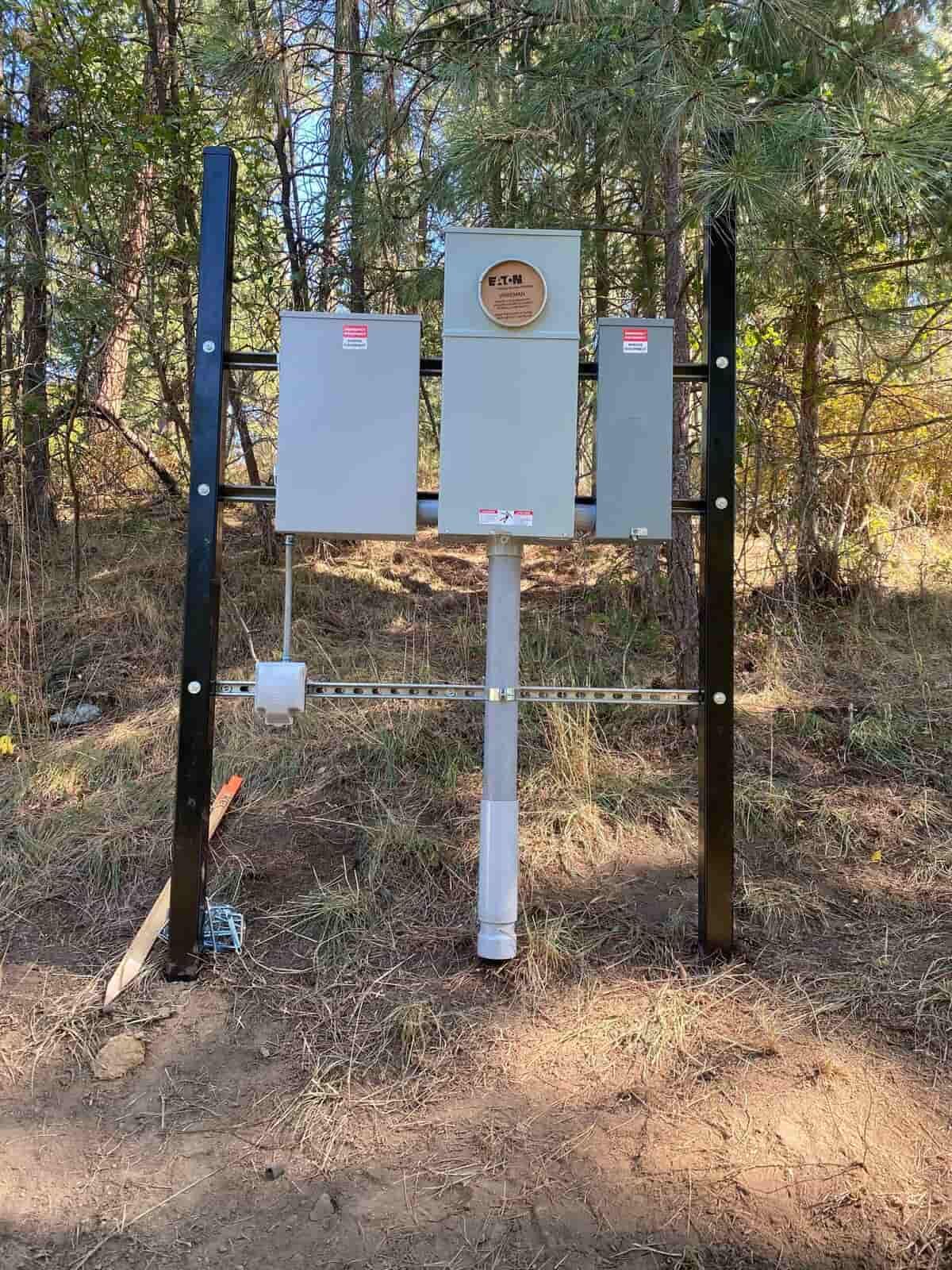 A electrical box is sitting on top of a pole in the middle of a forest.