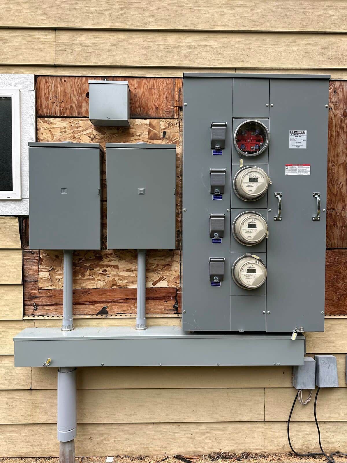 A gray electrical box is attached to the side of a house.