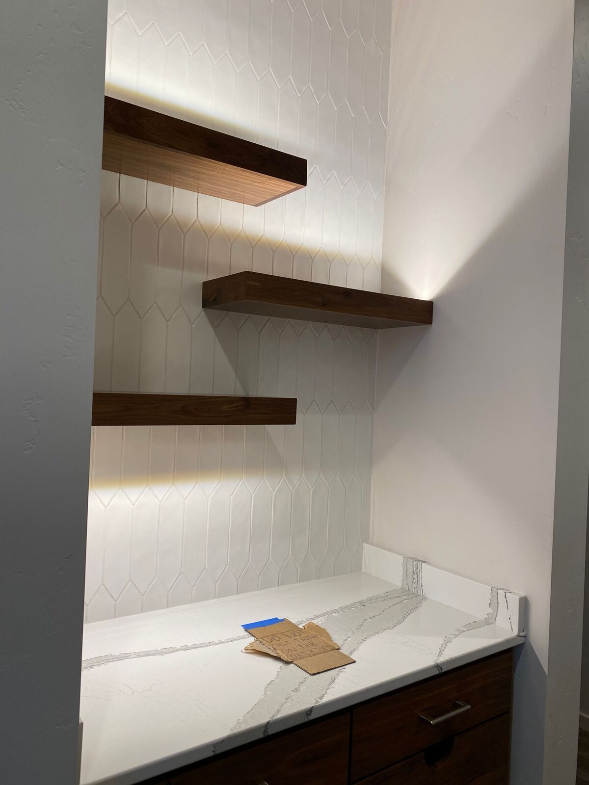 A kitchen with a marble counter top and wooden shelves.