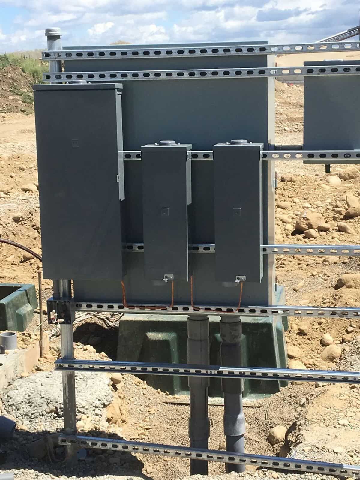 A large electrical box is sitting in the middle of a dirt field.