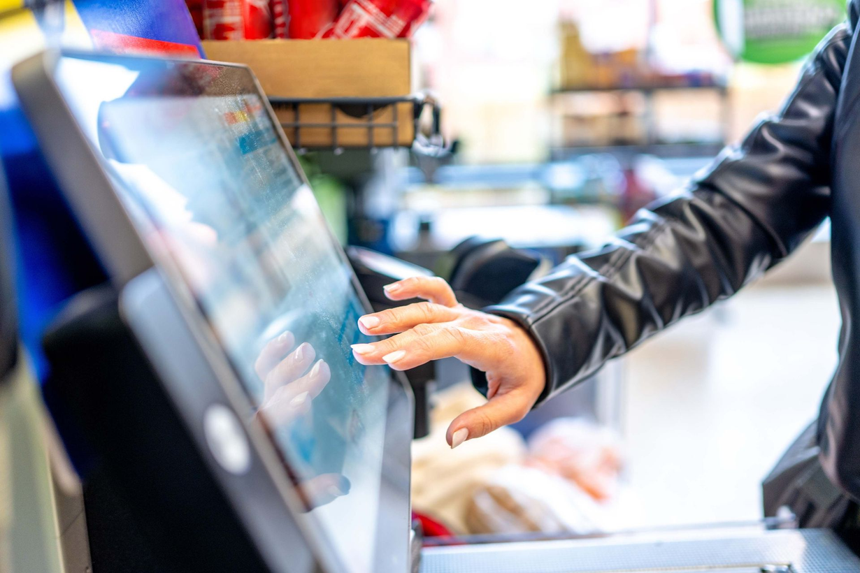 Person tapping a touchscreen payment terminal in a store checkout area