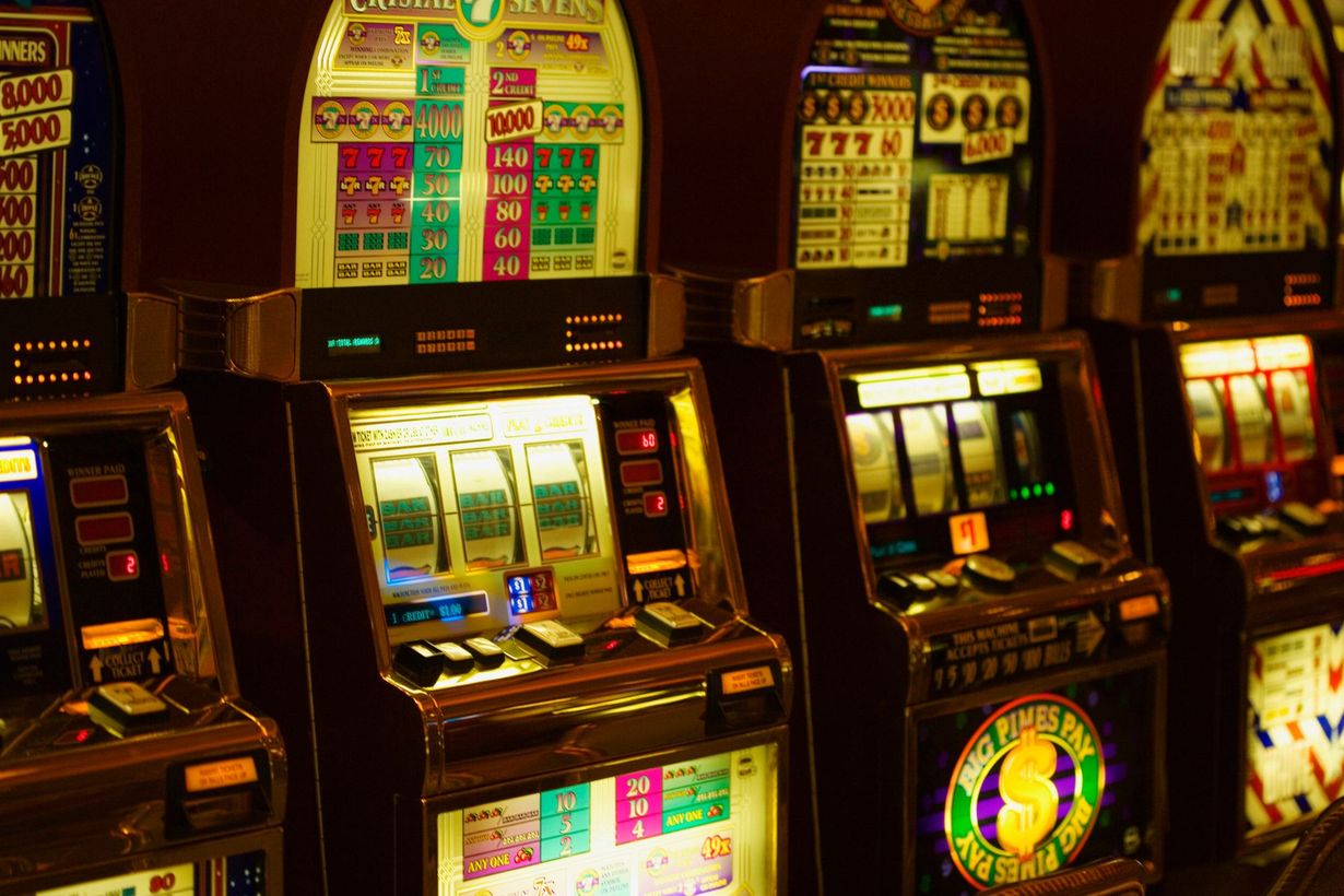 Row of illuminated slot machines in a dim casino, glowing with bright red, yellow, and green lights