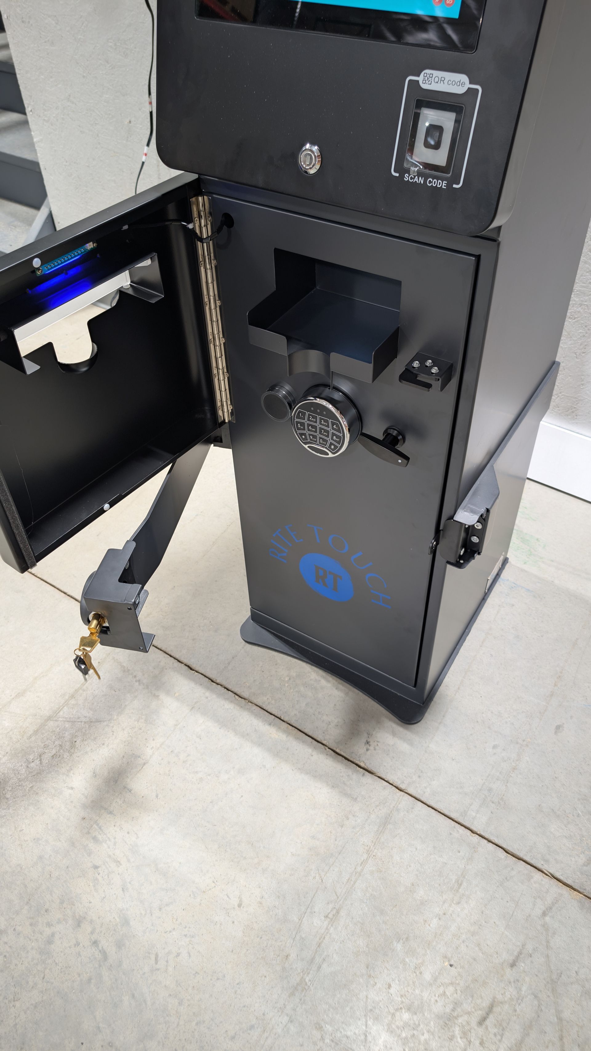 Black vending machine or kiosk with an open side panel and a wheel mechanism on a tiled floor.