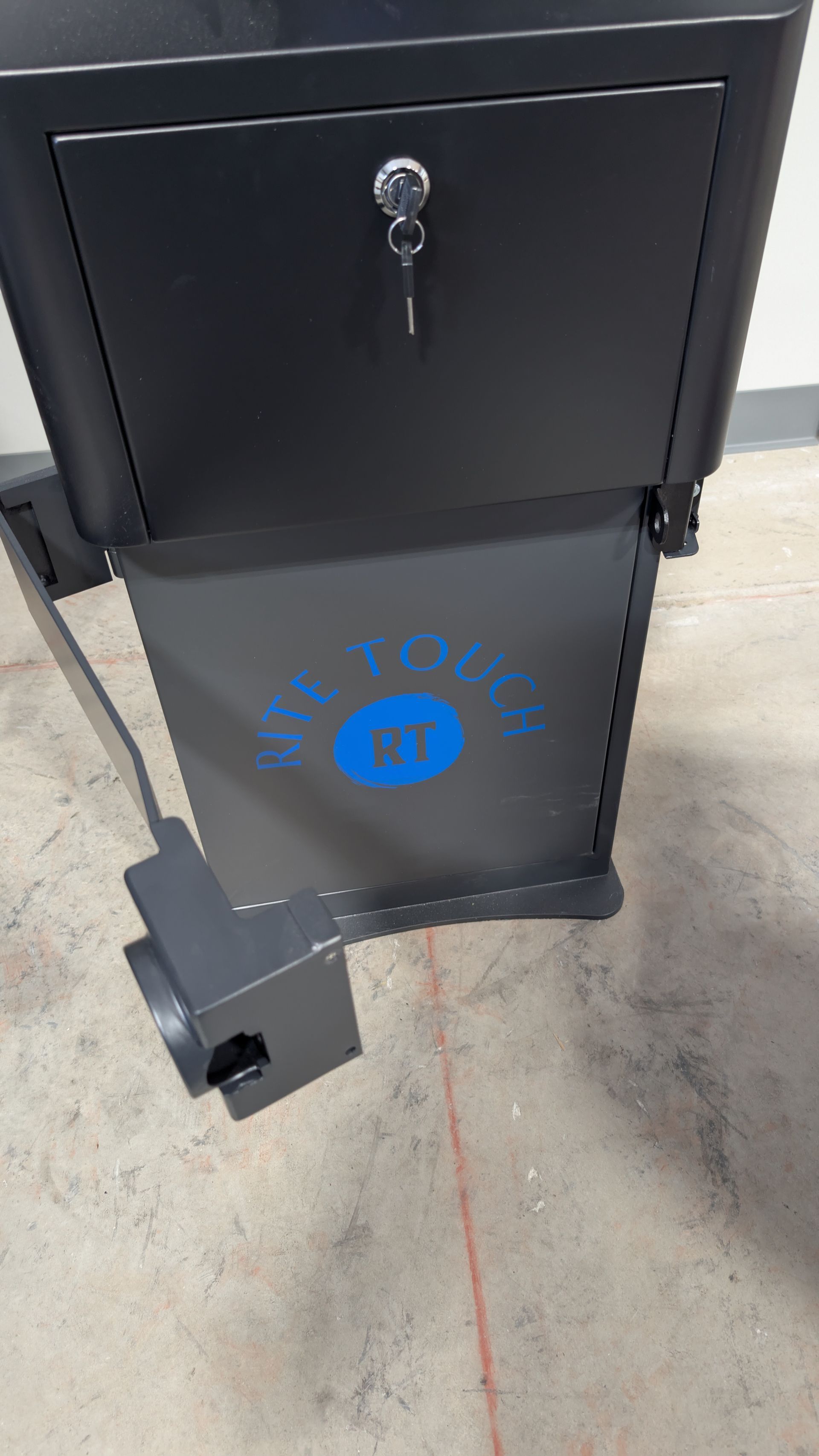 Black metal box with lock on a wheeled base, standing on a concrete floor.