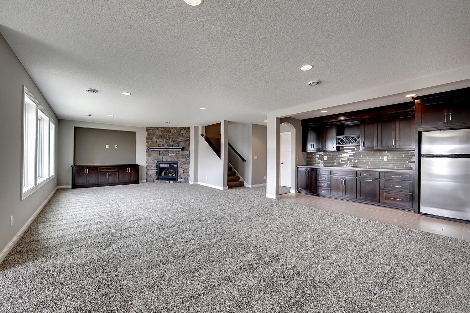 an empty basement with a fireplace and a kitchen