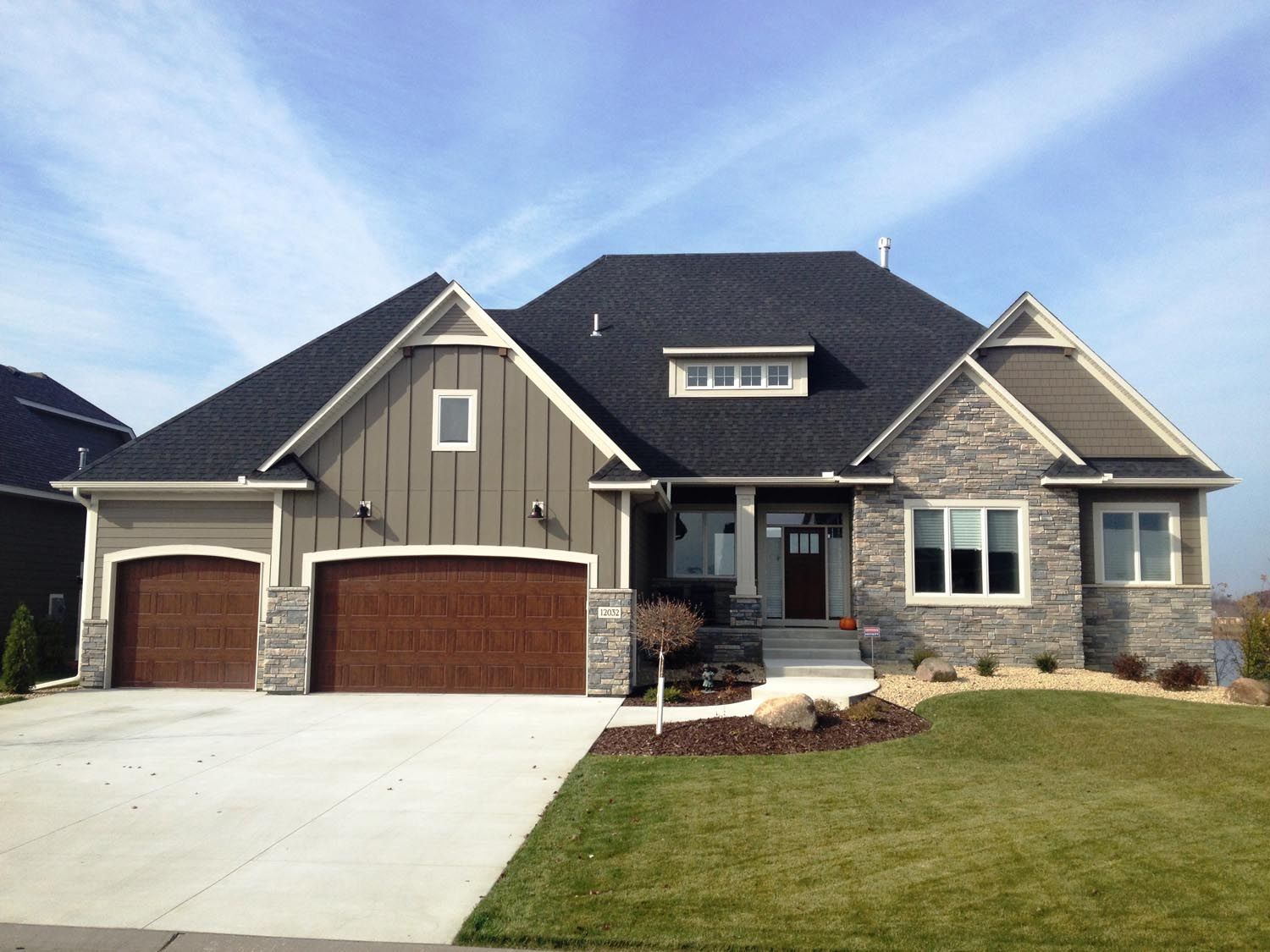 a large house with a black roof and brown garage doors