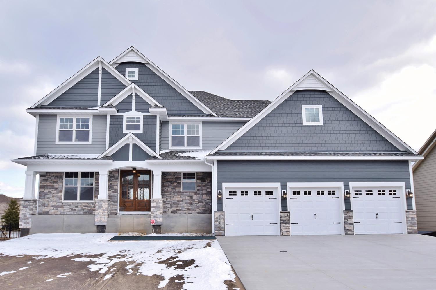 a large gray house with white garage doors and a snowy driveway