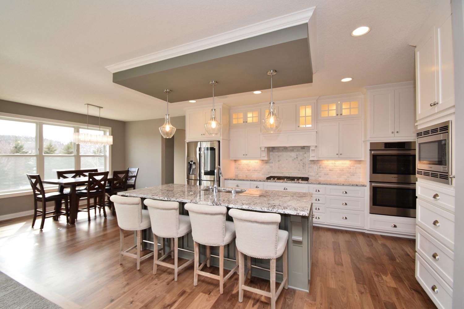 a kitchen with white cabinets, granite counter tops, stools and a large island