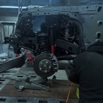 Car chassis being repaired in a workshop. A person is working on the suspension.