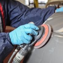 Person in blue gloves sanding a car with a power sander.