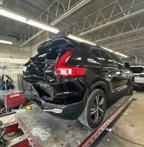 Black car with rear-end damage, in a repair shop.