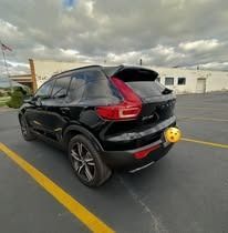 Black Volvo SUV parked on asphalt, yellow line, cloudy sky.