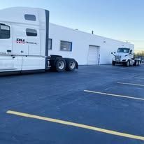 Two semi-trucks parked near a white commercial building with loading docks.