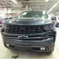 Gray Chevrolet Silverado truck front view, in an auto repair shop with missing front components.
