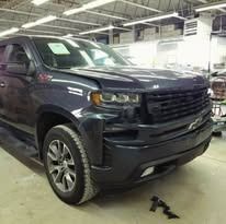Dark blue pickup truck in a repair shop; front view with damage to the hood and bumper.