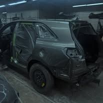 Grey SUV being repaired in a garage, missing rear bumper and door panels, with protective tape.