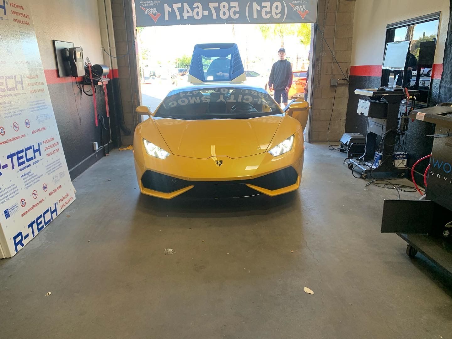 Yellow Lamborghini parked inside a garage, headlights on, door open. A person stands in the background.