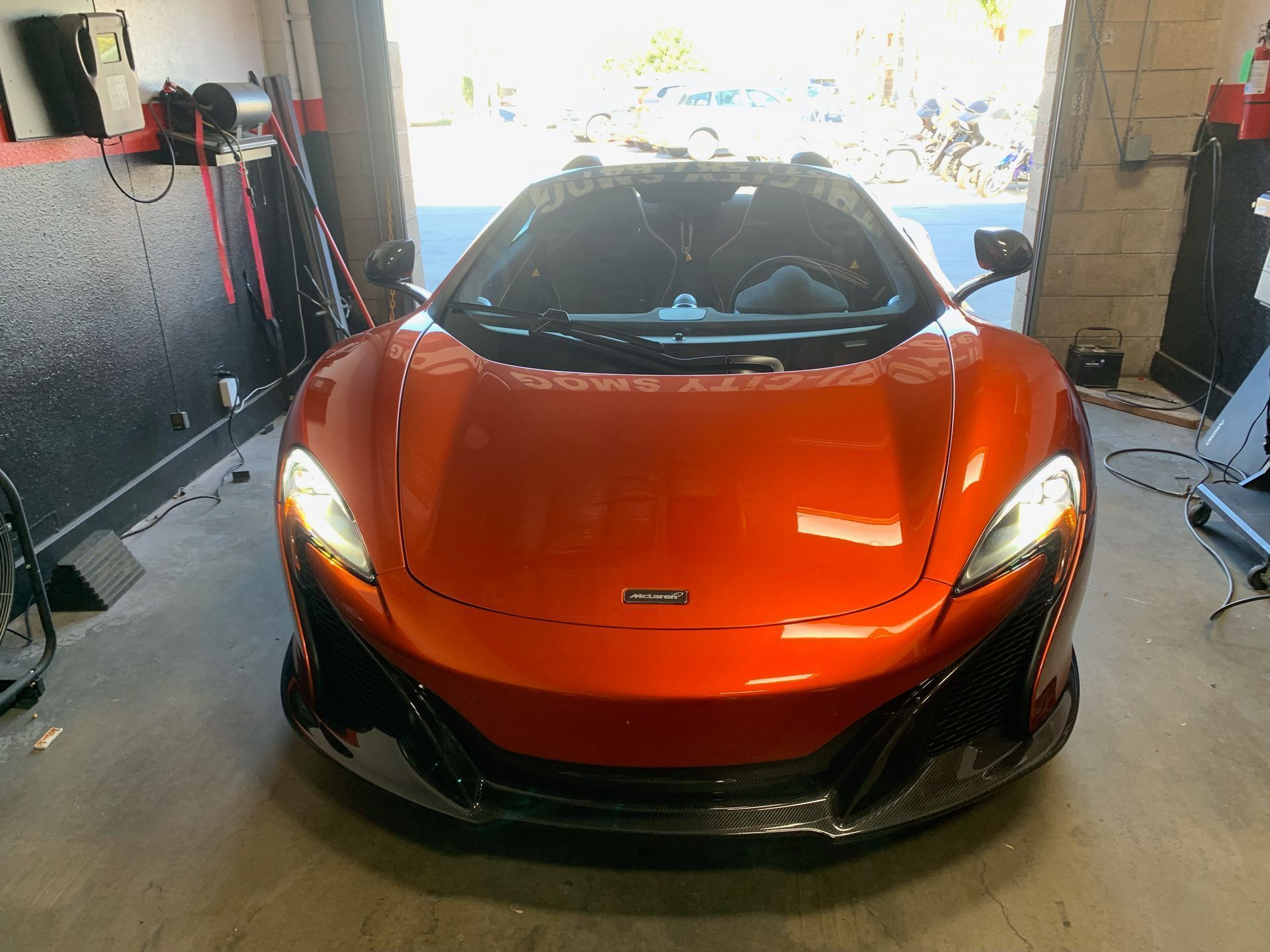Orange McLaren sports car in a garage with open door, headlights on.