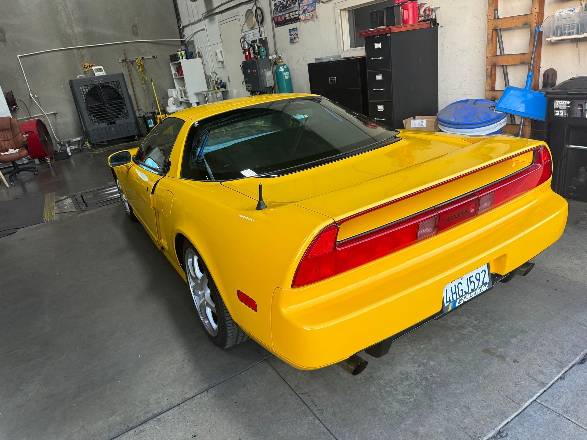 A bright yellow Honda NSX sports car is parked inside a garage. The car has a rear spoiler and chrome wheels.