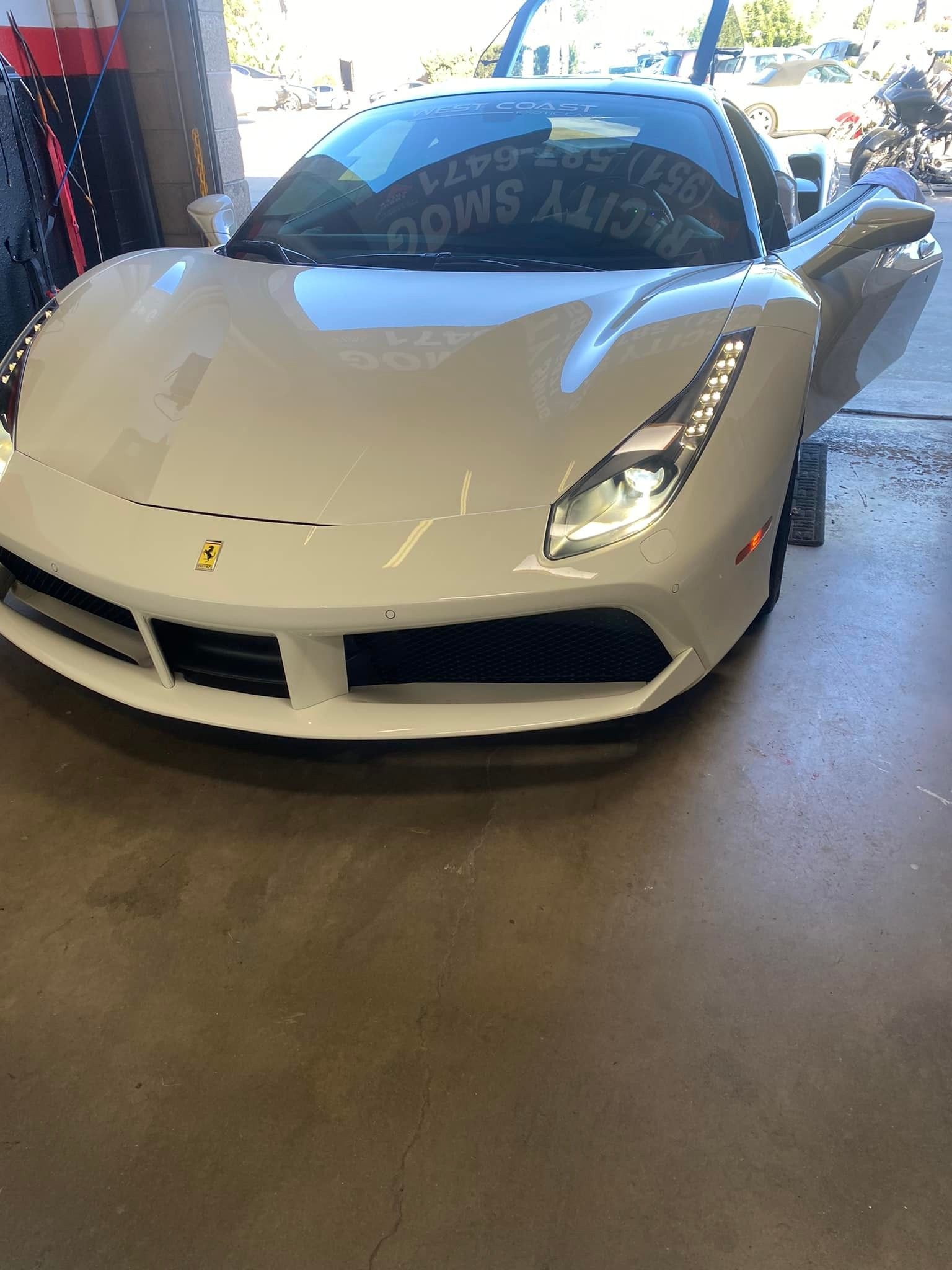 White Ferrari sports car with doors open, parked indoors on a concrete surface.