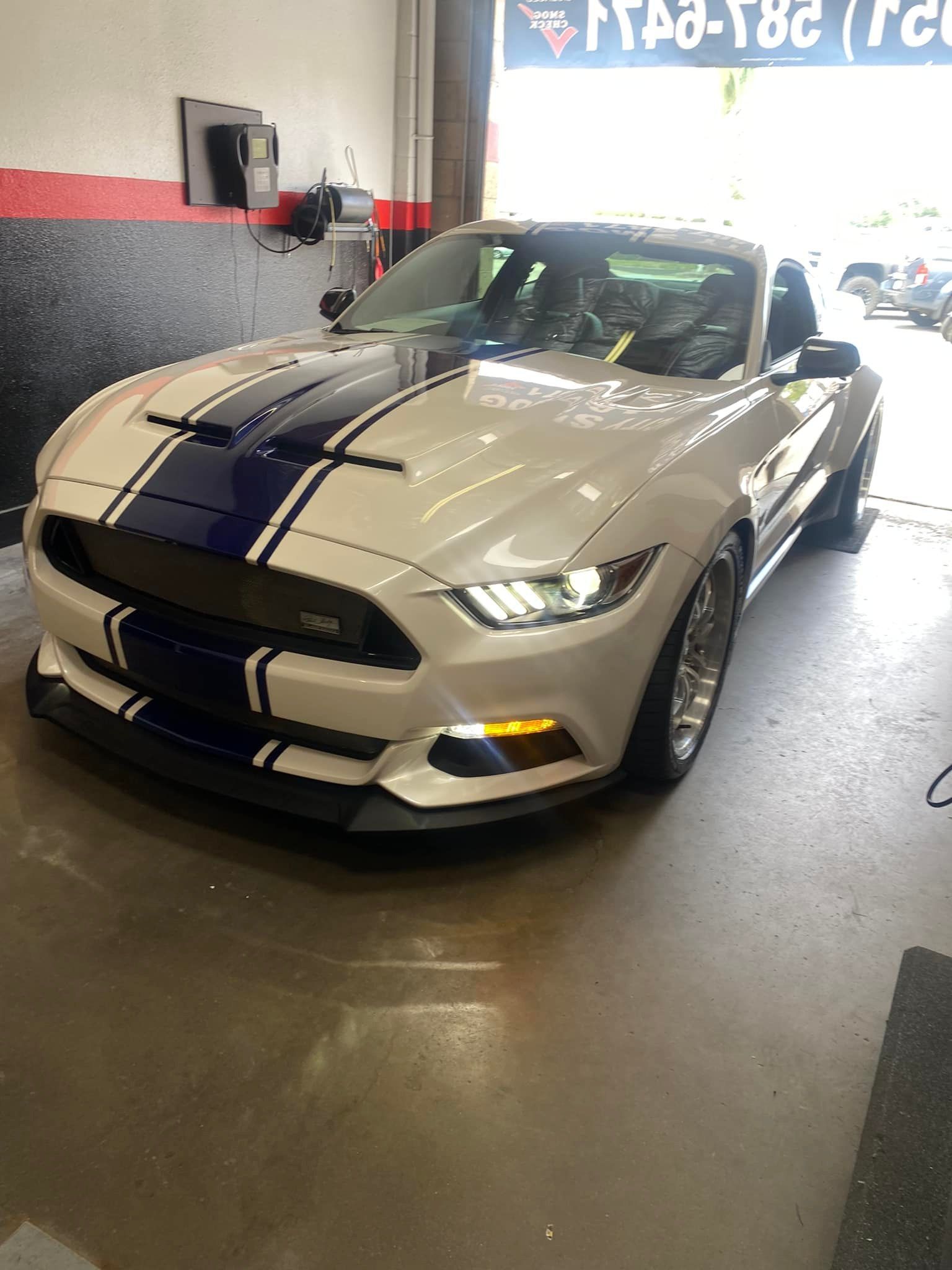 White Ford Mustang with blue racing stripes inside a garage.