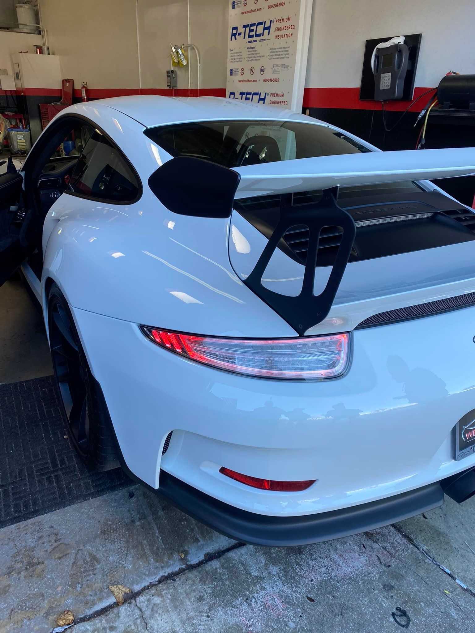 White Porsche sports car with a large rear spoiler, parked in a garage.
