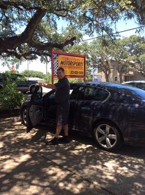 A man is standing next to a car in front of a sign